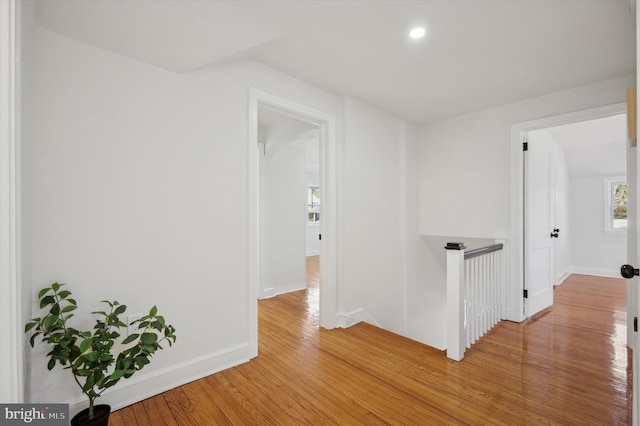 corridor with an upstairs landing, light wood-style floors, and baseboards