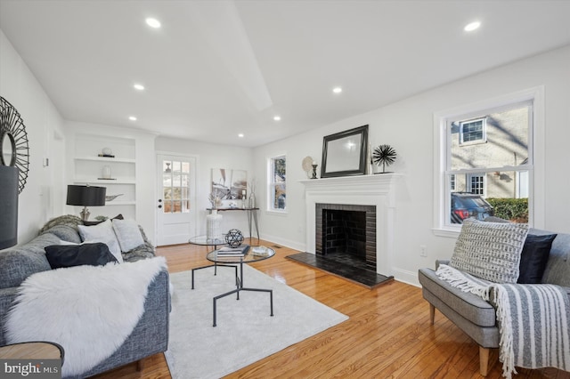 living area with built in features, a fireplace, plenty of natural light, and wood finished floors