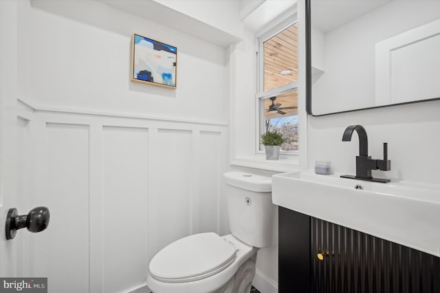 bathroom with a wainscoted wall, toilet, and a decorative wall