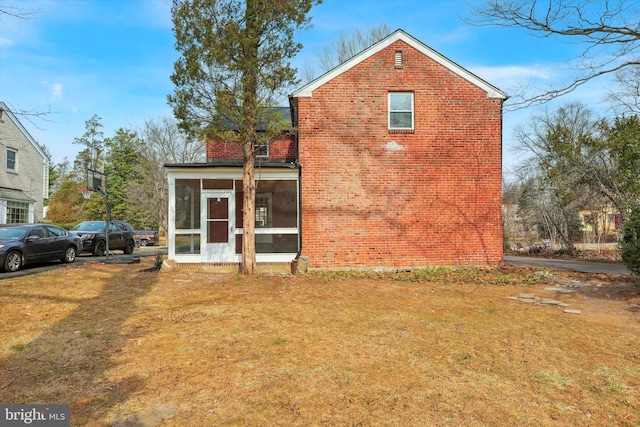 back of property featuring brick siding, a yard, and a sunroom