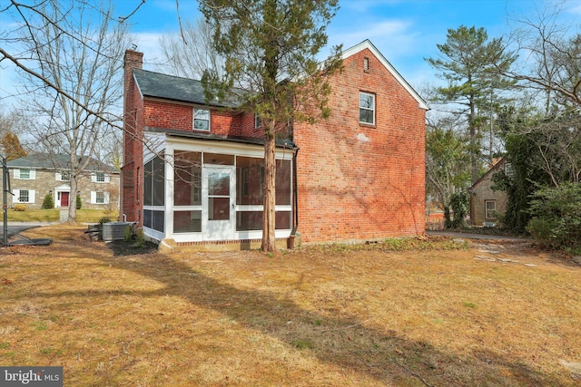 back of house with a yard, brick siding, a sunroom, and a chimney