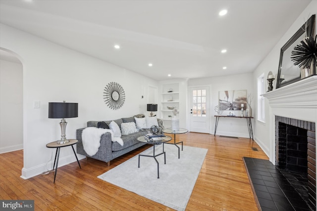 living area featuring a fireplace, wood finished floors, arched walkways, and baseboards