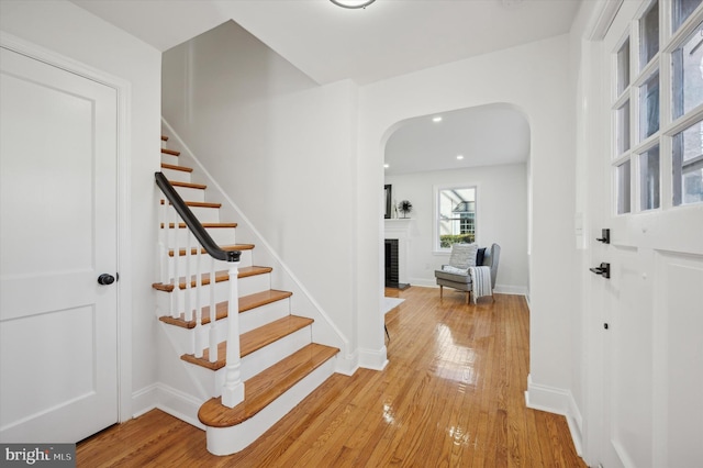 staircase with arched walkways, a fireplace, baseboards, and hardwood / wood-style floors