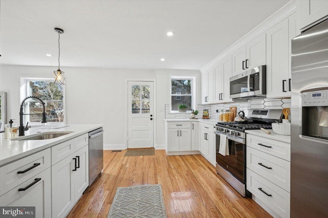 kitchen with light wood finished floors, a sink, decorative backsplash, light countertops, and stainless steel appliances