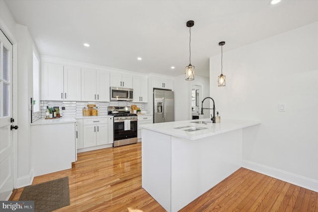 kitchen featuring light wood-type flooring, a peninsula, white cabinets, stainless steel appliances, and a sink