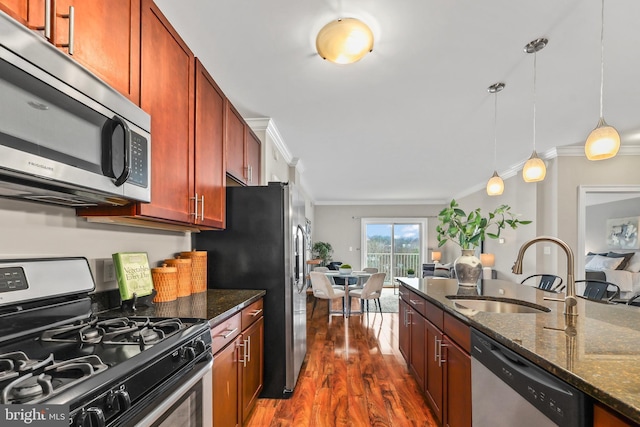 kitchen featuring sink, decorative light fixtures, dark stone counters, ornamental molding, and stainless steel appliances