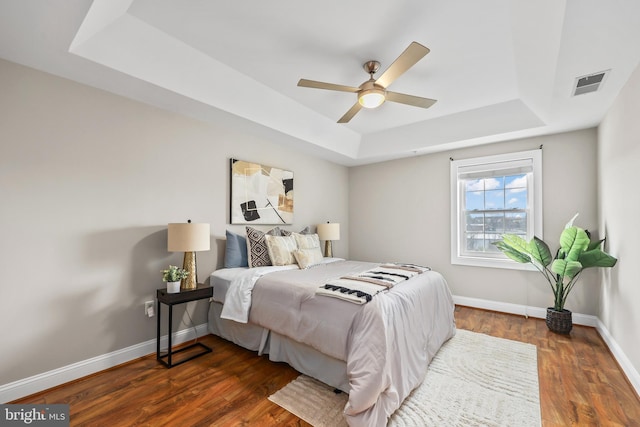 bedroom featuring a raised ceiling, dark wood-type flooring, and ceiling fan