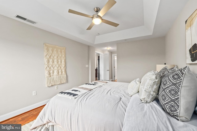 bedroom with a tray ceiling, ceiling fan, and hardwood / wood-style flooring