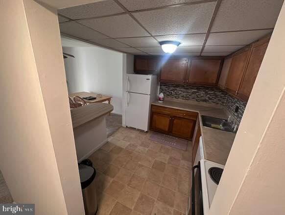 kitchen featuring white refrigerator, a paneled ceiling, sink, and decorative backsplash