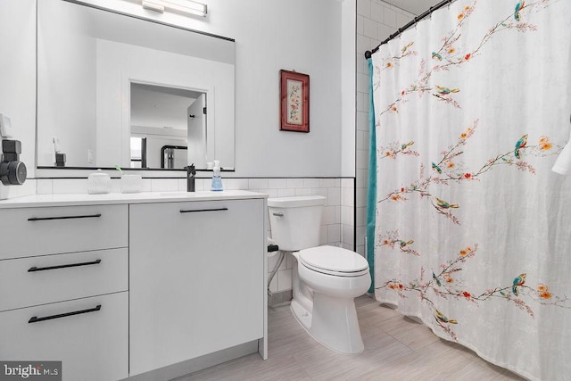 bathroom featuring vanity, toilet, and tile walls