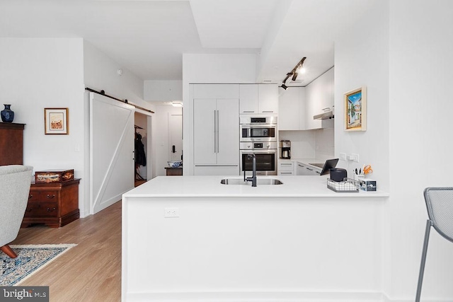 kitchen featuring sink, white cabinetry, kitchen peninsula, a barn door, and light wood-type flooring