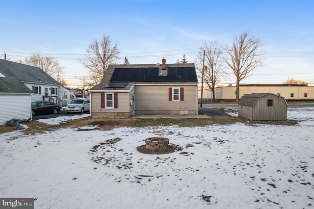 snow covered house featuring a storage unit, a fire pit, and solar panels