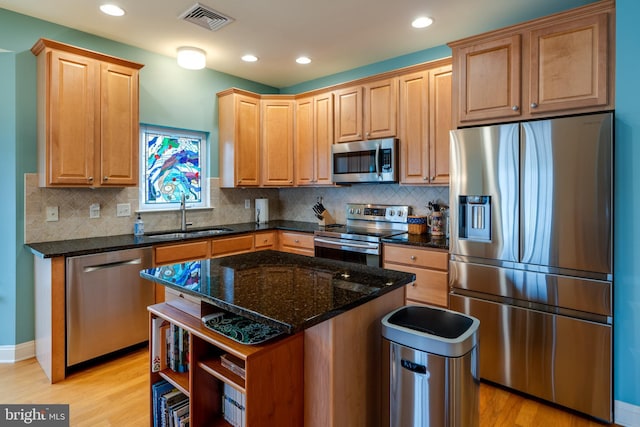 kitchen with a kitchen island, sink, dark stone countertops, stainless steel appliances, and light wood-type flooring