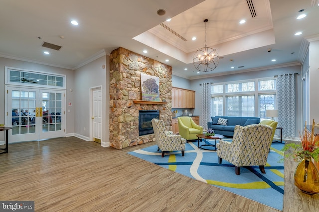 living room with a stone fireplace, ornamental molding, a raised ceiling, light wood-type flooring, and french doors