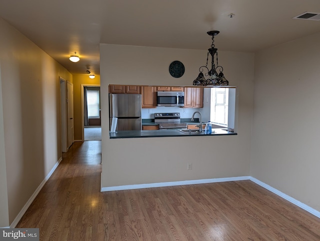 kitchen with sink, appliances with stainless steel finishes, wood-type flooring, decorative light fixtures, and kitchen peninsula