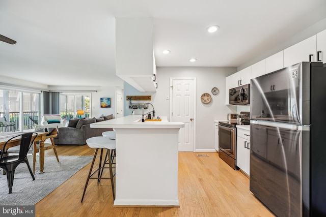 kitchen featuring white cabinetry, appliances with stainless steel finishes, a kitchen breakfast bar, and light hardwood / wood-style flooring