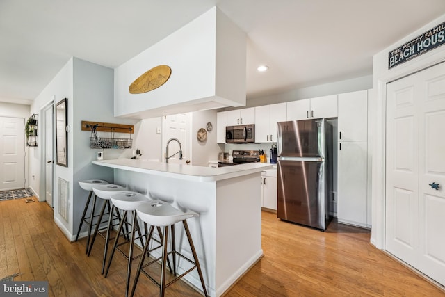 kitchen with a breakfast bar, appliances with stainless steel finishes, light hardwood / wood-style floors, white cabinets, and kitchen peninsula