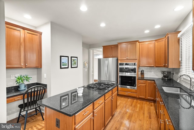 kitchen with sink, stainless steel appliances, built in desk, a kitchen island, and dark stone counters