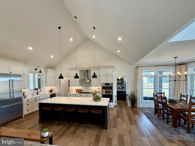 kitchen with wall chimney exhaust hood, white cabinetry, appliances with stainless steel finishes, pendant lighting, and a large island