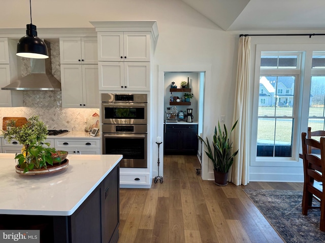 kitchen with white cabinetry, stainless steel appliances, decorative backsplash, decorative light fixtures, and light wood-type flooring