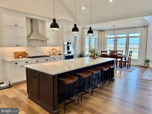 kitchen with wall chimney range hood, gas cooktop, white cabinetry, a spacious island, and stainless steel double oven