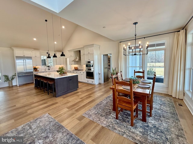 dining space featuring sink, a chandelier, high vaulted ceiling, and light wood-type flooring