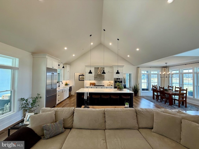 living room featuring high vaulted ceiling, sink, hardwood / wood-style floors, and a notable chandelier