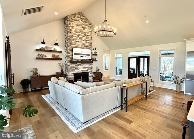 living room with an inviting chandelier, high vaulted ceiling, a stone fireplace, and hardwood / wood-style floors