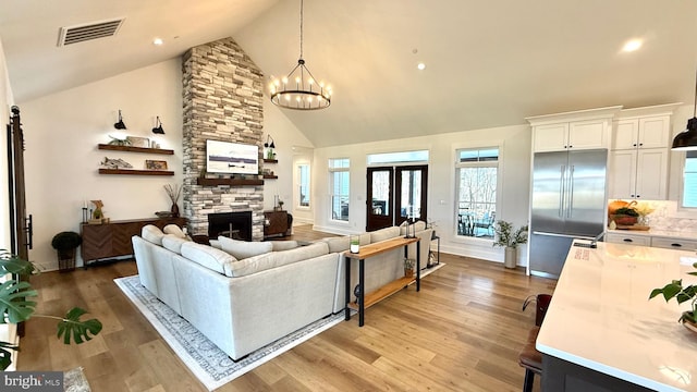 living room with a notable chandelier, a stone fireplace, high vaulted ceiling, and light wood-type flooring