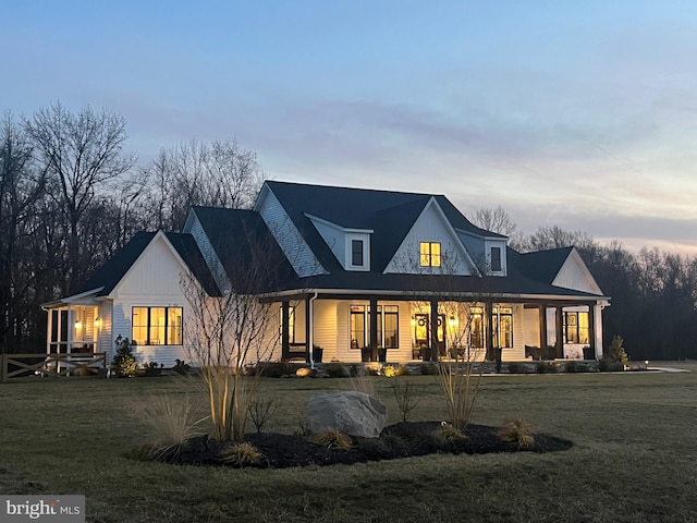 back house at dusk featuring a porch and a yard