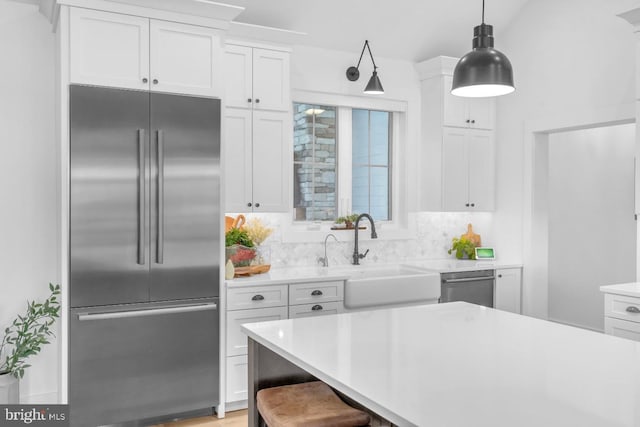 kitchen featuring a kitchen bar, sink, white cabinetry, decorative light fixtures, and stainless steel appliances