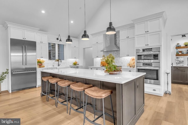 kitchen with decorative light fixtures, white cabinets, stainless steel appliances, wall chimney range hood, and a spacious island