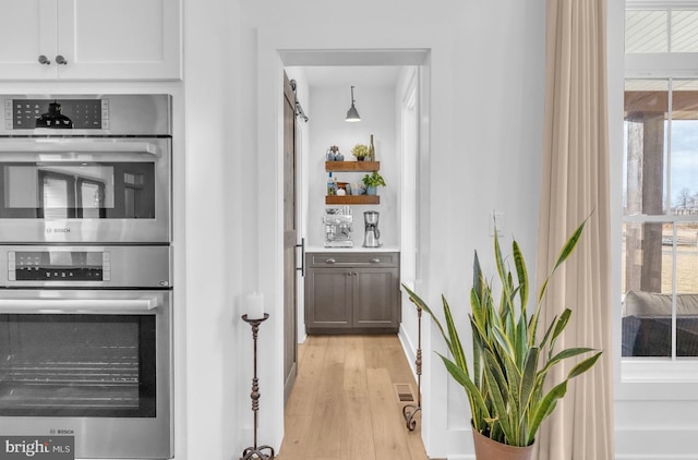 interior space with white cabinetry, stainless steel double oven, and light hardwood / wood-style flooring