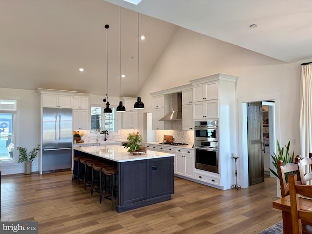 kitchen with appliances with stainless steel finishes, white cabinetry, hanging light fixtures, a center island, and wall chimney exhaust hood