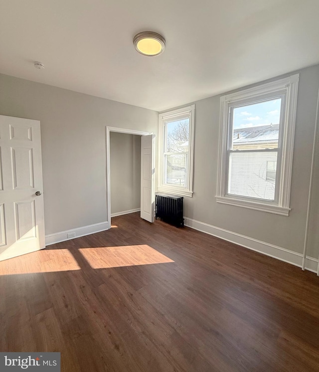 unfurnished bedroom with dark wood-type flooring, radiator heating unit, and a closet