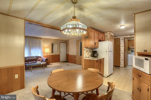 kitchen featuring pendant lighting, white appliances, washer / dryer, and wood walls