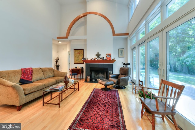 living room with a tile fireplace, wood-type flooring, and a towering ceiling