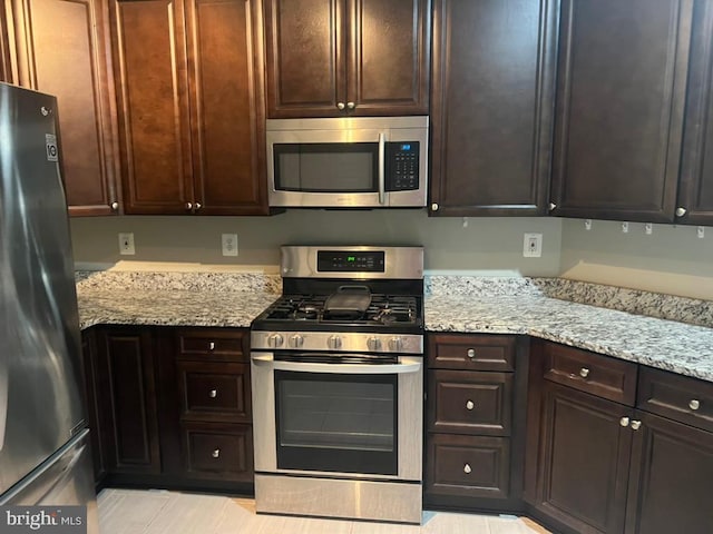 kitchen featuring light stone counters, dark brown cabinetry, and appliances with stainless steel finishes