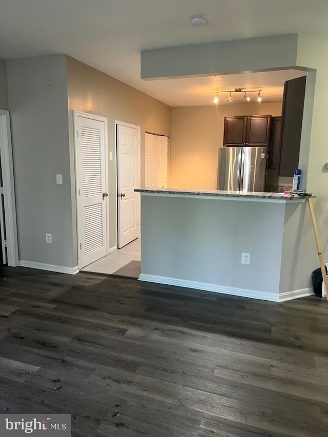 kitchen with dark brown cabinets, dark wood-type flooring, stainless steel refrigerator, and kitchen peninsula