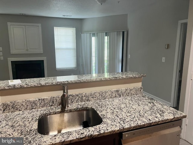 details featuring light stone countertops, sink, stainless steel dishwasher, and a textured ceiling