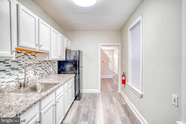 kitchen with black fridge, sink, white cabinets, and decorative backsplash