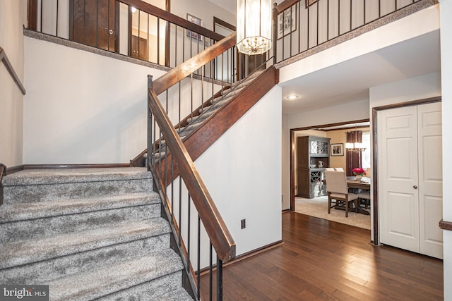 stairway with baseboards, a notable chandelier, a towering ceiling, and hardwood / wood-style floors