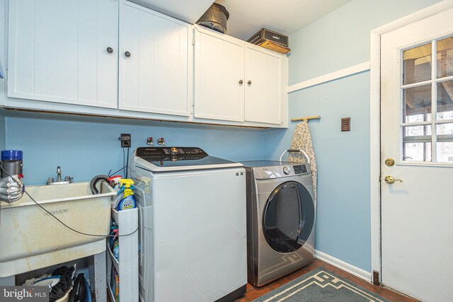 washroom with cabinet space, baseboards, washer and clothes dryer, and a sink