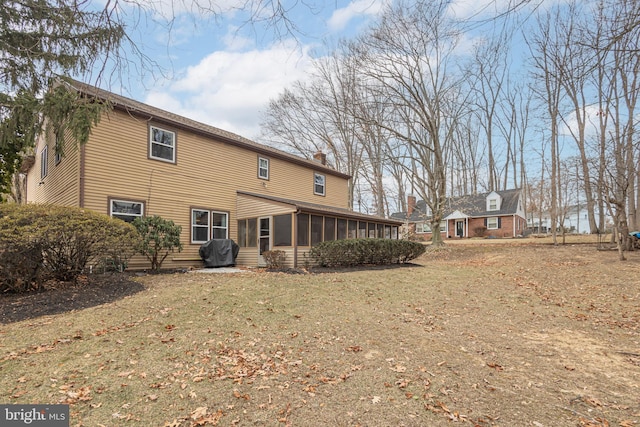 back of property featuring a sunroom, a chimney, and a yard