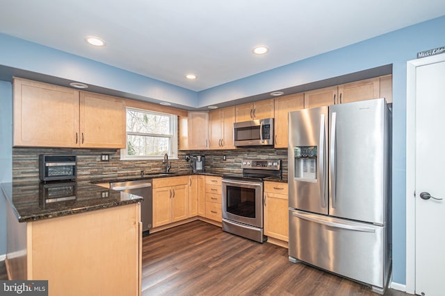 kitchen with dark wood-style floors, stainless steel appliances, tasteful backsplash, light brown cabinetry, and dark stone countertops