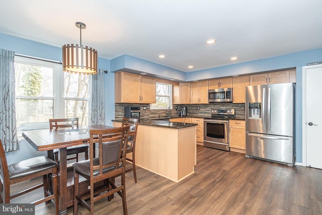 kitchen featuring a peninsula, hanging light fixtures, appliances with stainless steel finishes, backsplash, and dark wood finished floors