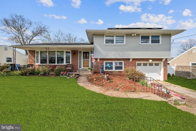 split level home with a porch, a garage, a front yard, and solar panels