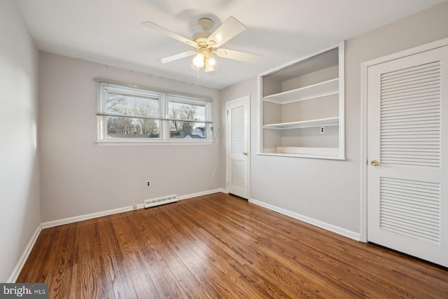 unfurnished bedroom featuring wood finished floors, a ceiling fan, multiple closets, visible vents, and baseboards