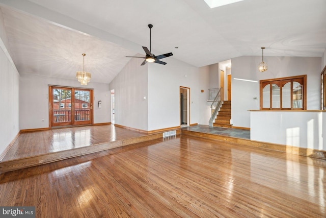 unfurnished living room with visible vents, wood-type flooring, stairway, vaulted ceiling, and ceiling fan with notable chandelier