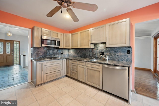 kitchen featuring stainless steel appliances, tasteful backsplash, light brown cabinetry, a sink, and dark stone counters